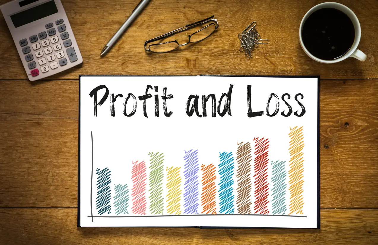 may 7,, overhead top view of profit and loss written in book on desk with a coloured bar chart and trend line desk has coffee cup glasses pen and calculator