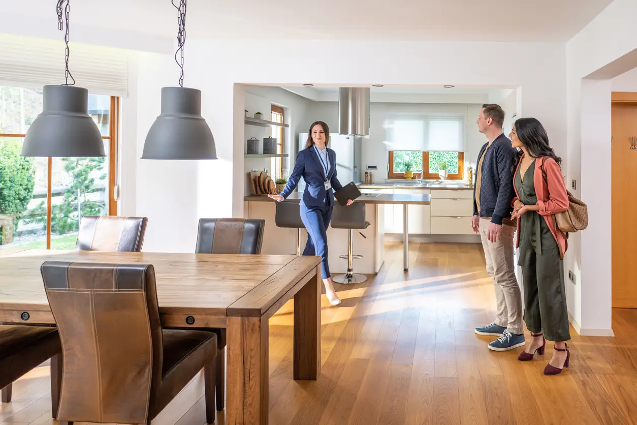may 7,, young female real estate agent showing couple modern kitchen and dining room in apartment