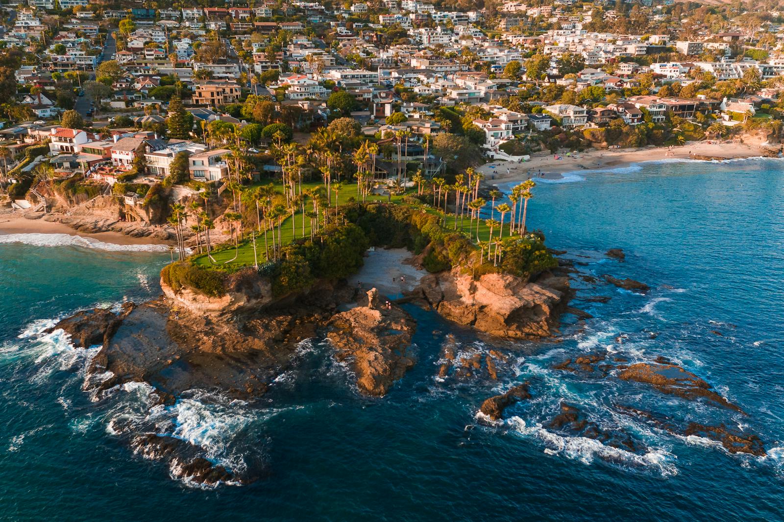 Stunning aerial view of Laguna Beach with rocky coastline, palm trees, and ocean waves.
